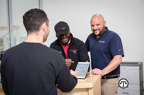 Three men standing at a desk looking at a tablet.