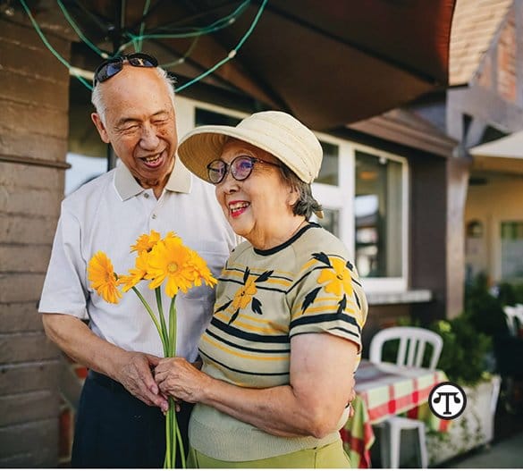 An asian couple holding flowers in front of a restaurant.