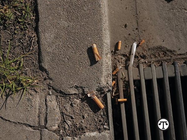 Cigarette butts on the ground next to a grate.